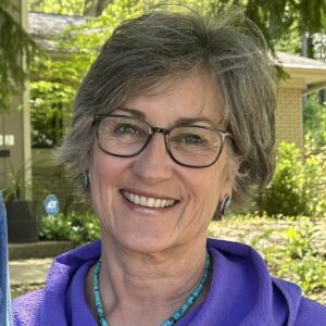 Joni Kinsey wearing a purple top and turquoise necklace, outdoors.