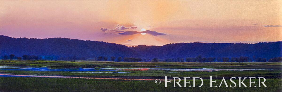 Sunset over grassy wetlands with distant hills and a colorful sky reflected in the water.
